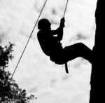 man hanging on rope climbing a cliff
