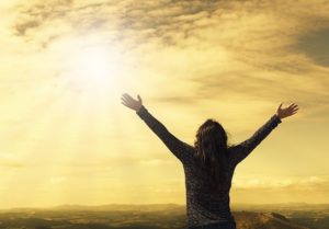 Person with arms raised looking up at the bright sun