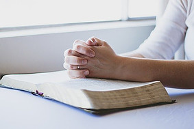 praying with hands clasped on a bible